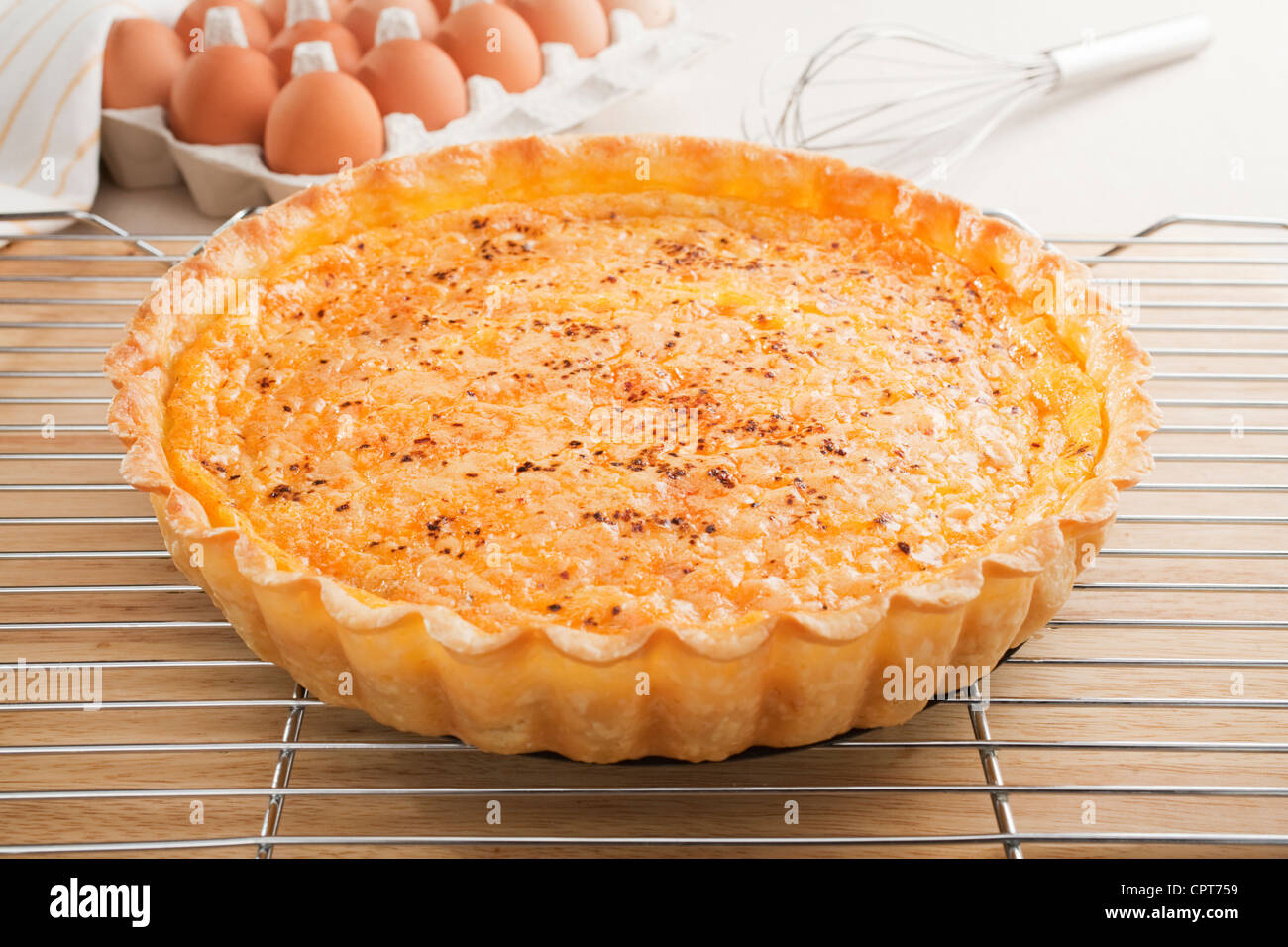 Salmon quiche, fresh from the oven, cooling on a wire rack, eggs and whisk in background. Stock Photo