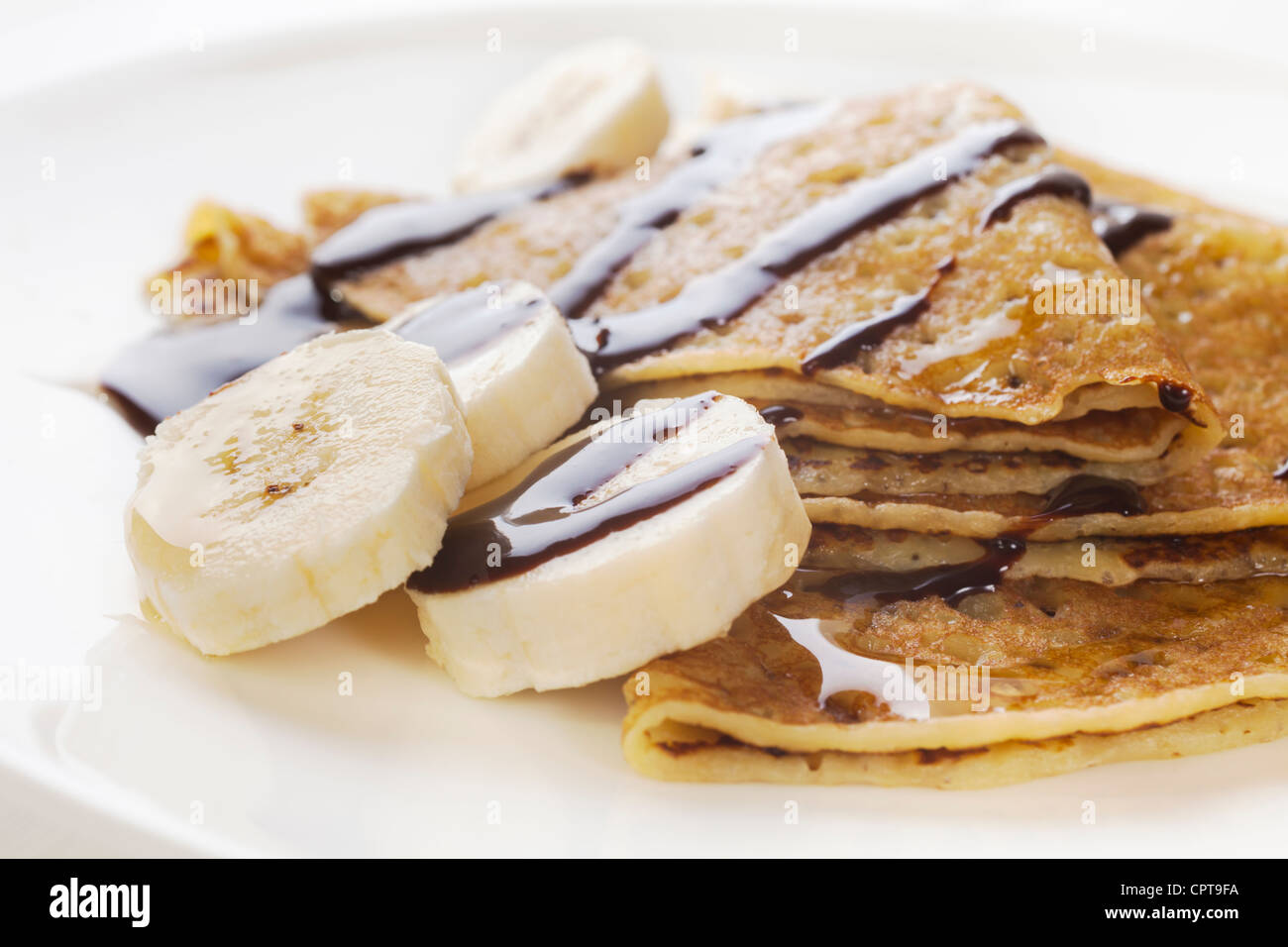 Crepes or pancakes, with banana, maple syrup and chocolate sauce. Stock Photo