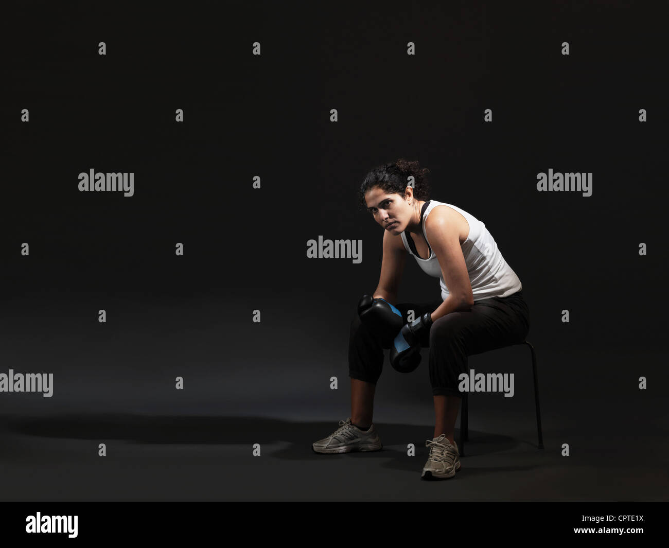 Portrait of female boxer sitting against black background Stock Photo