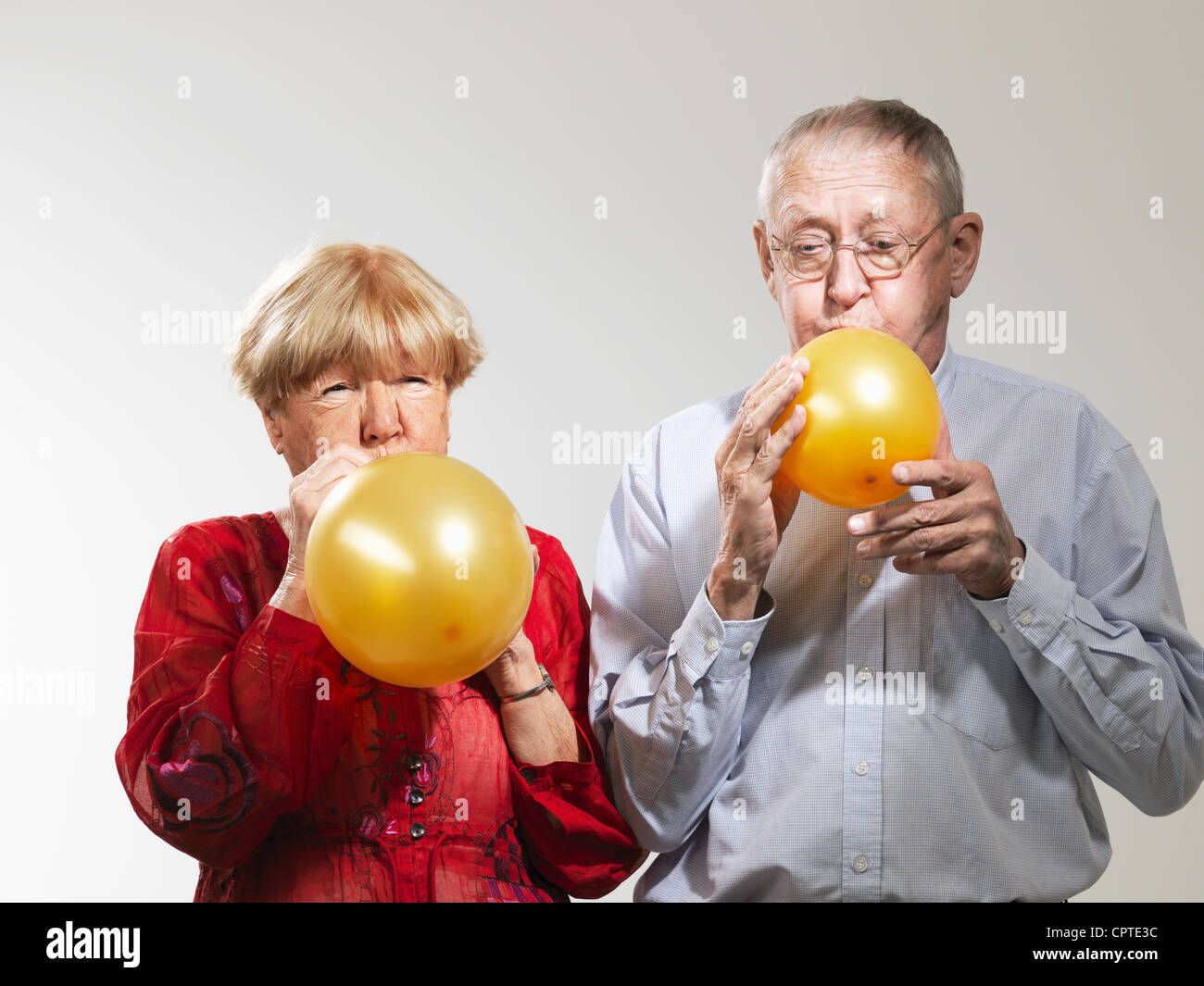 Senior blowing up balloons against white background Stock Photo
