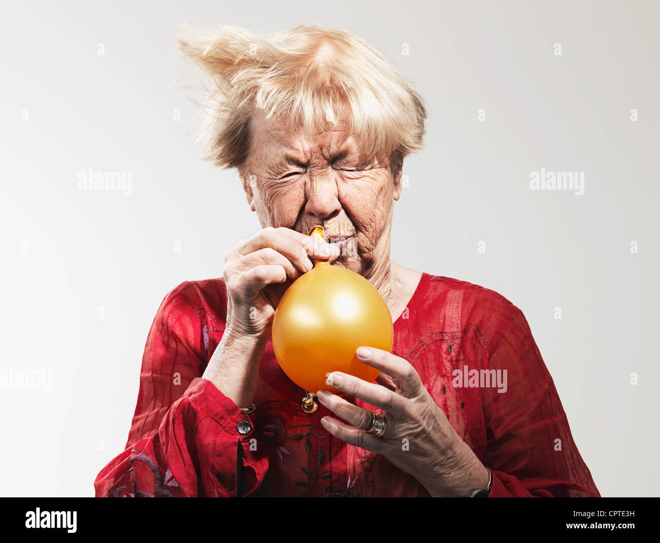Senior woman deflating a balloon against white background Stock Photo