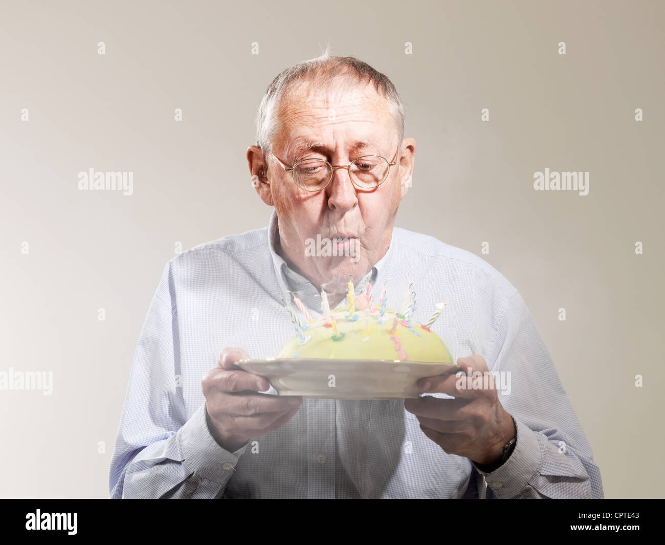 Senior man blowing out candles on brithday cake against white background Stock Photo