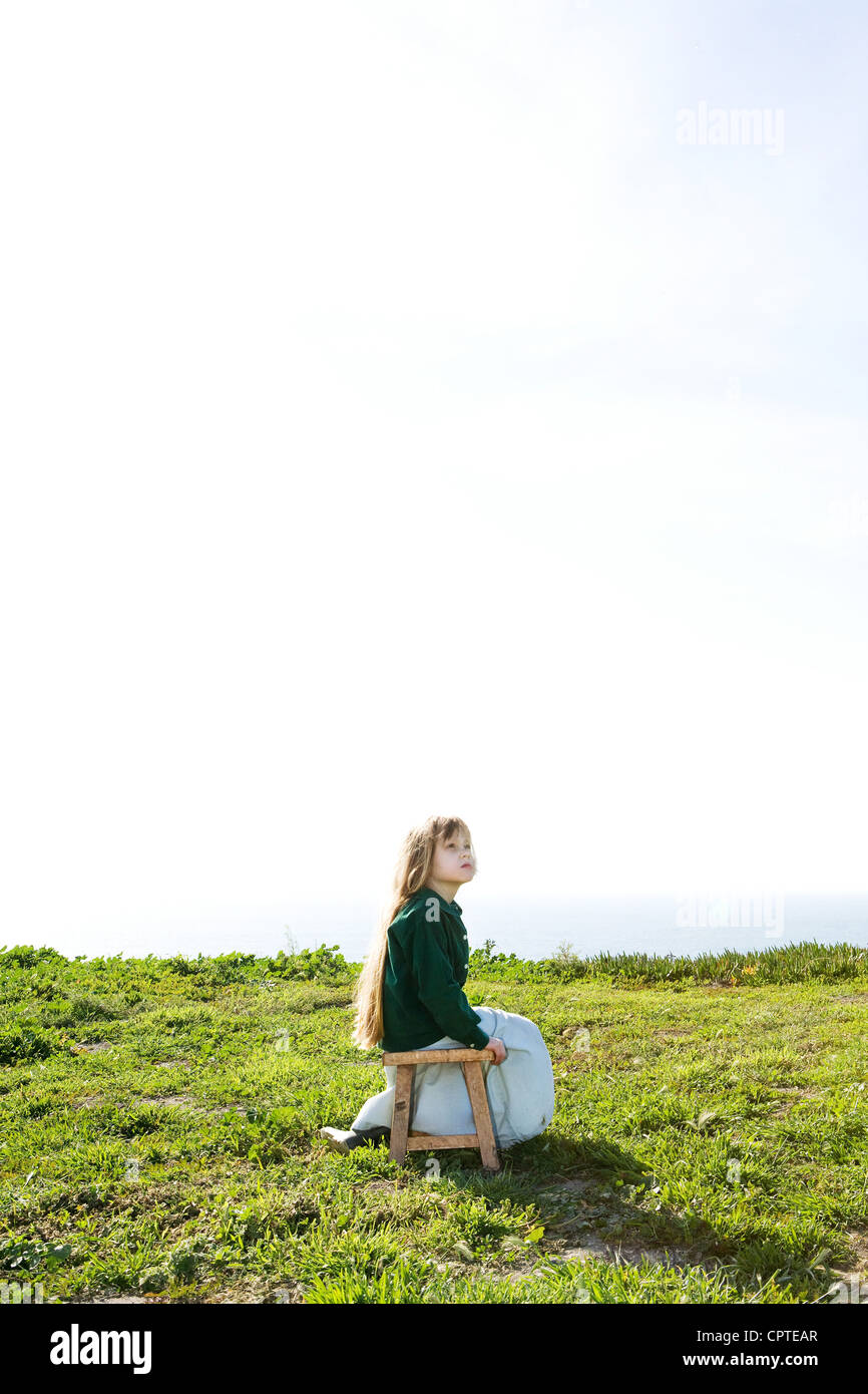Girl sitting alone in field under bright sky Stock Photo