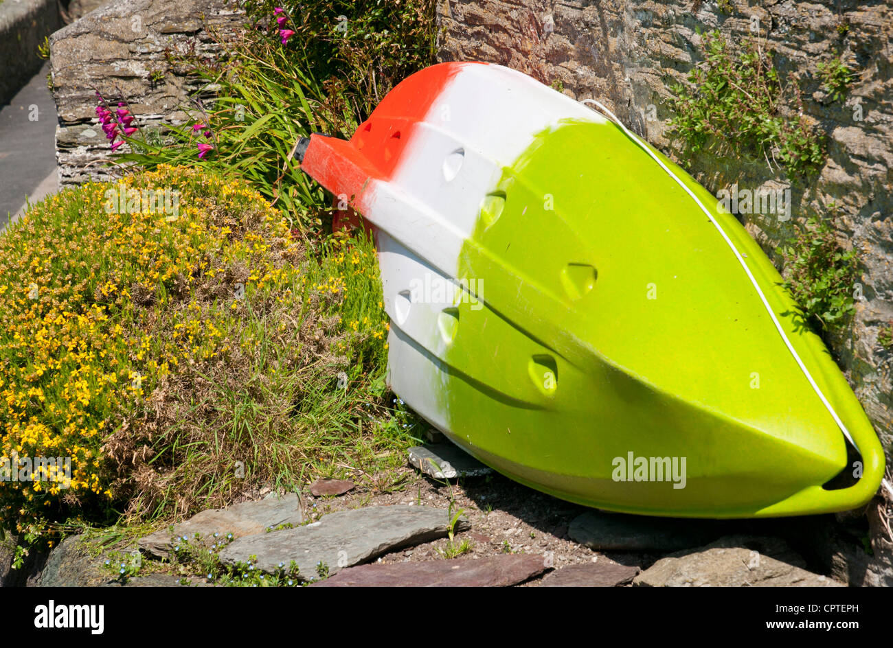 Red, white and green striped small boat outside cottage in fishing village of Polperro, Cornwall, UK Stock Photo