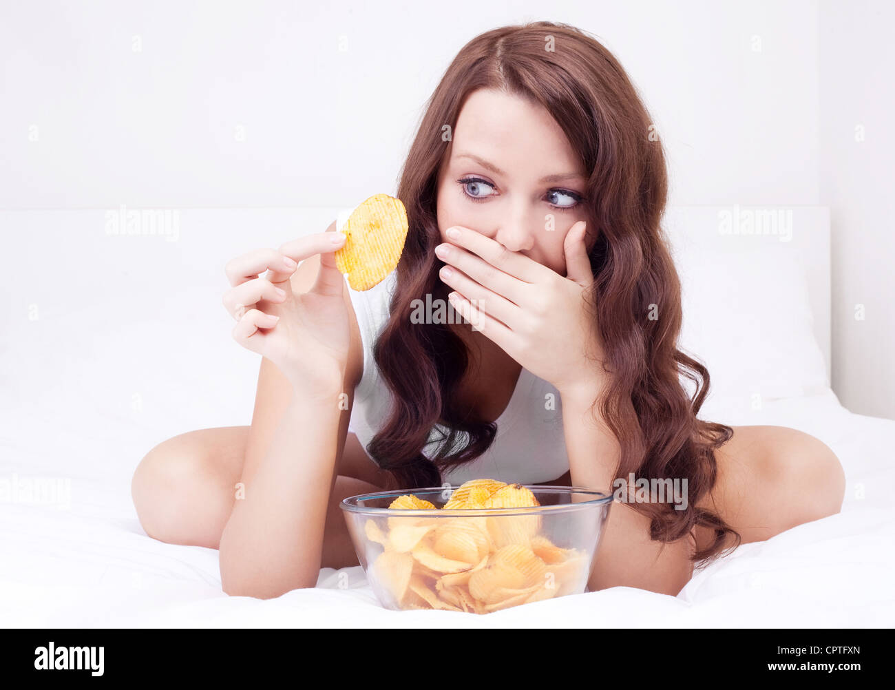 pretty woman eating potato chips in bed at home and scared of gaining