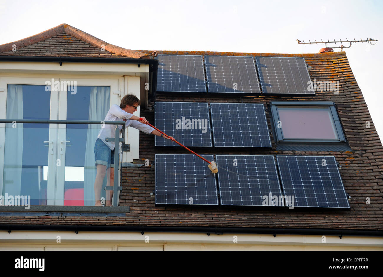 Woman cleaning dust of her solar panels with a broom on roof of domestic home Sussex UK Stock