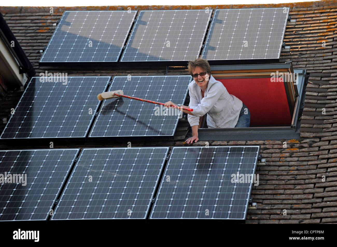 Woman cleaning dust of her solar panels with a broom on roof of