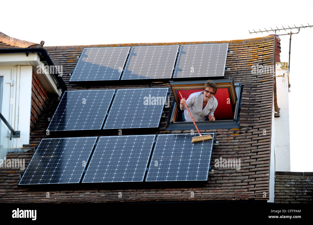 Woman cleaning dust of her solar panels with a broom on roof of domestic home Sussex UK Stock