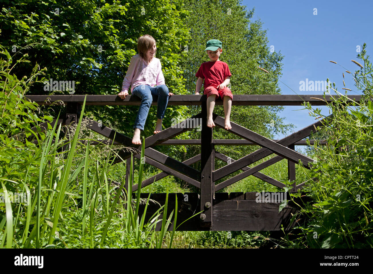 girl and boy sitting on the railing of a wooden bridge Stock Photo - Alamy