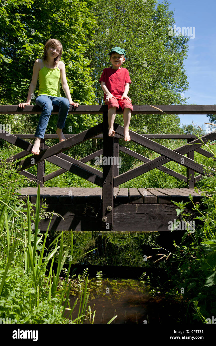 girl and boy sitting on the railing of a wooden bridge Stock Photo - Alamy