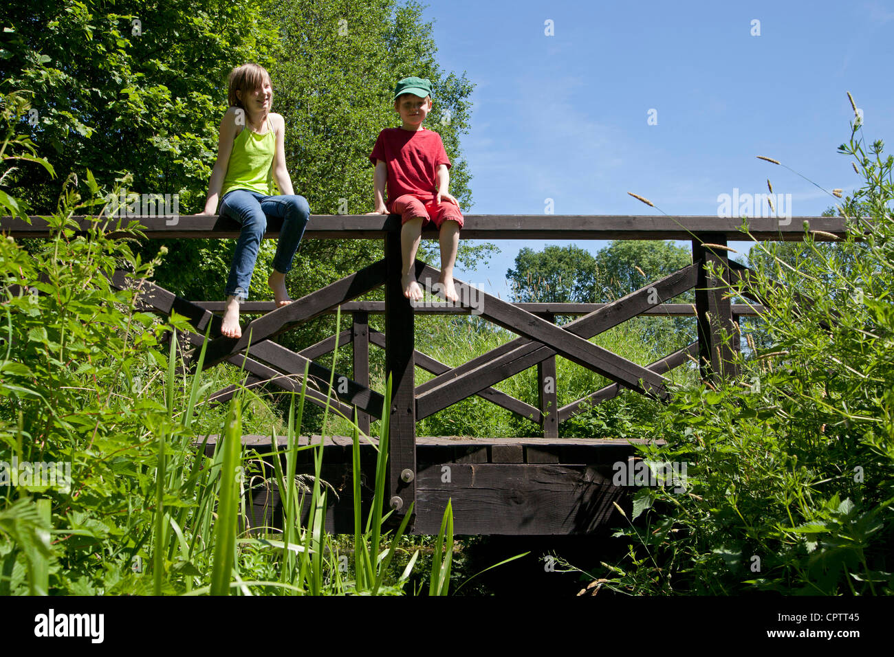 girl and boy sitting on the railing of a wooden bridge Stock Photo - Alamy