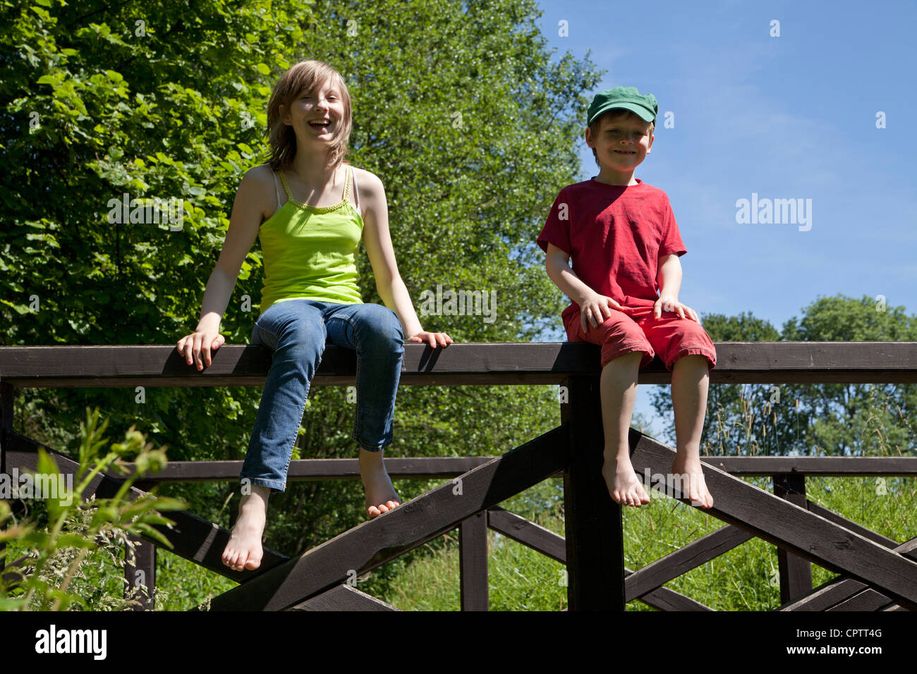 girl and boy sitting on the railing of a wooden bridge Stock Photo - Alamy
