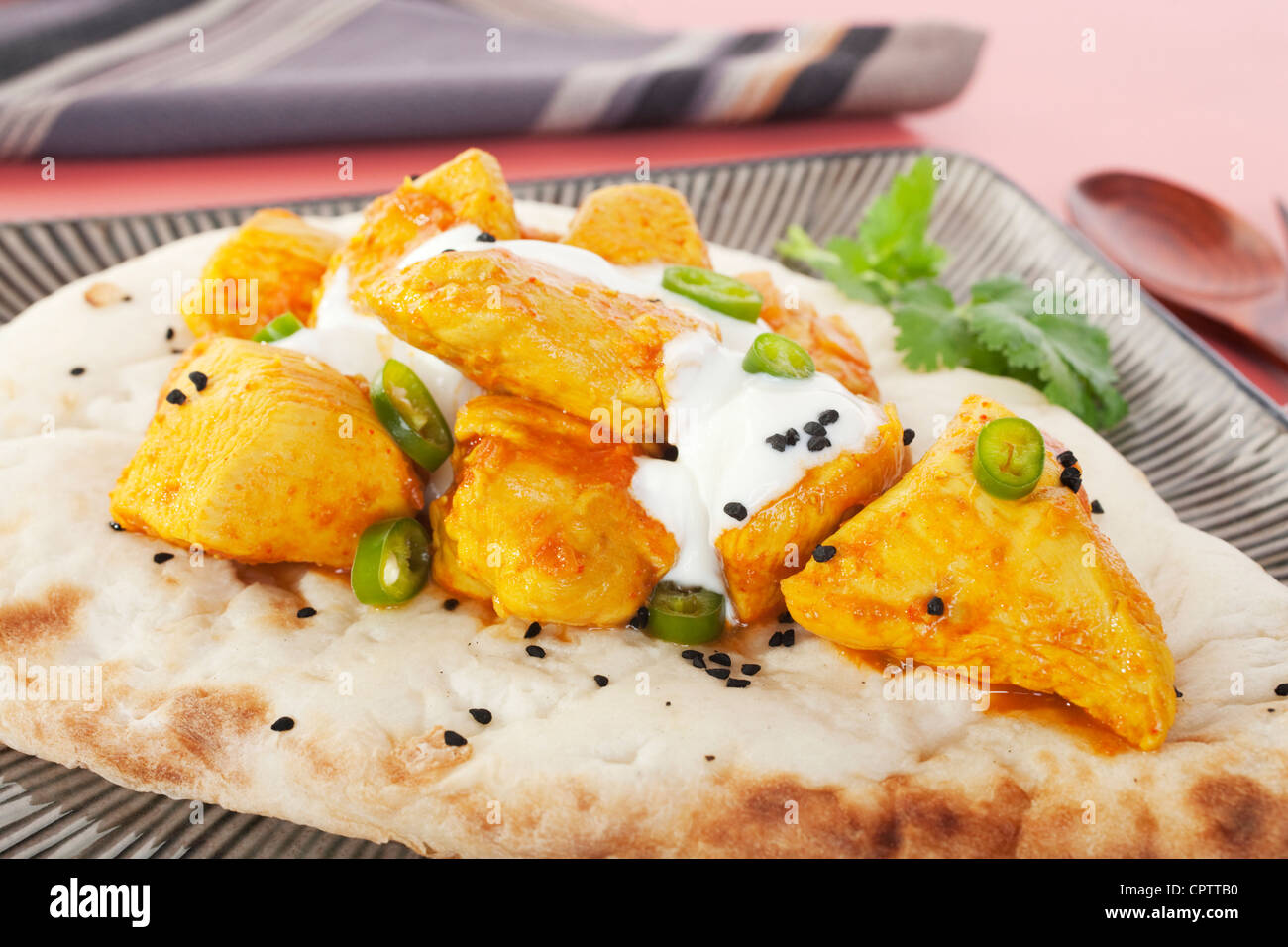 Chicken Madras curry on Indian naan bread, topped with yoghurt, chilli and kalonji seeds. Stock Photo