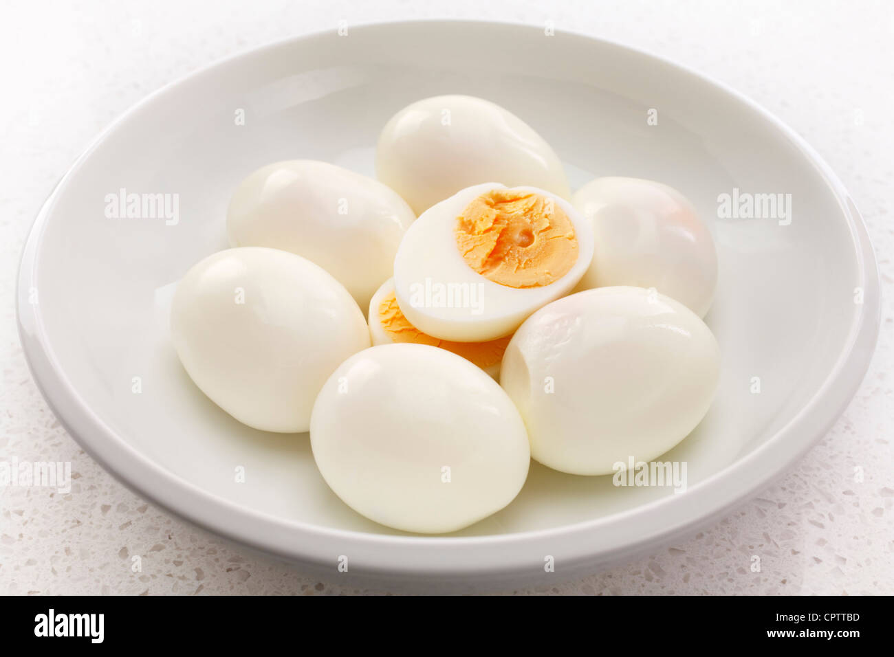 Seven hard boiled eggs in a white bowl, one cut into halves. Stock Photo