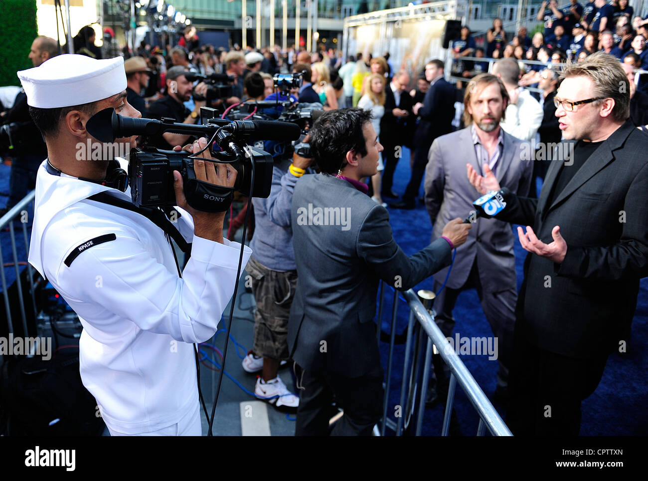 Mass Communication Specialist 3rd Class David Hooper, films an interview between a KTLA Channel 5 reporter and writers of the movie “Battleship,' Jon and Erich Hoeber, on the 'blue' carpet at the premiere of the film. Universal Pictures gave service members the celebrity treatment alongside cast members of the movie and invited them to attend the special screening of the film prior to its release in more than 3,000 theaters nationwide. Stock Photo