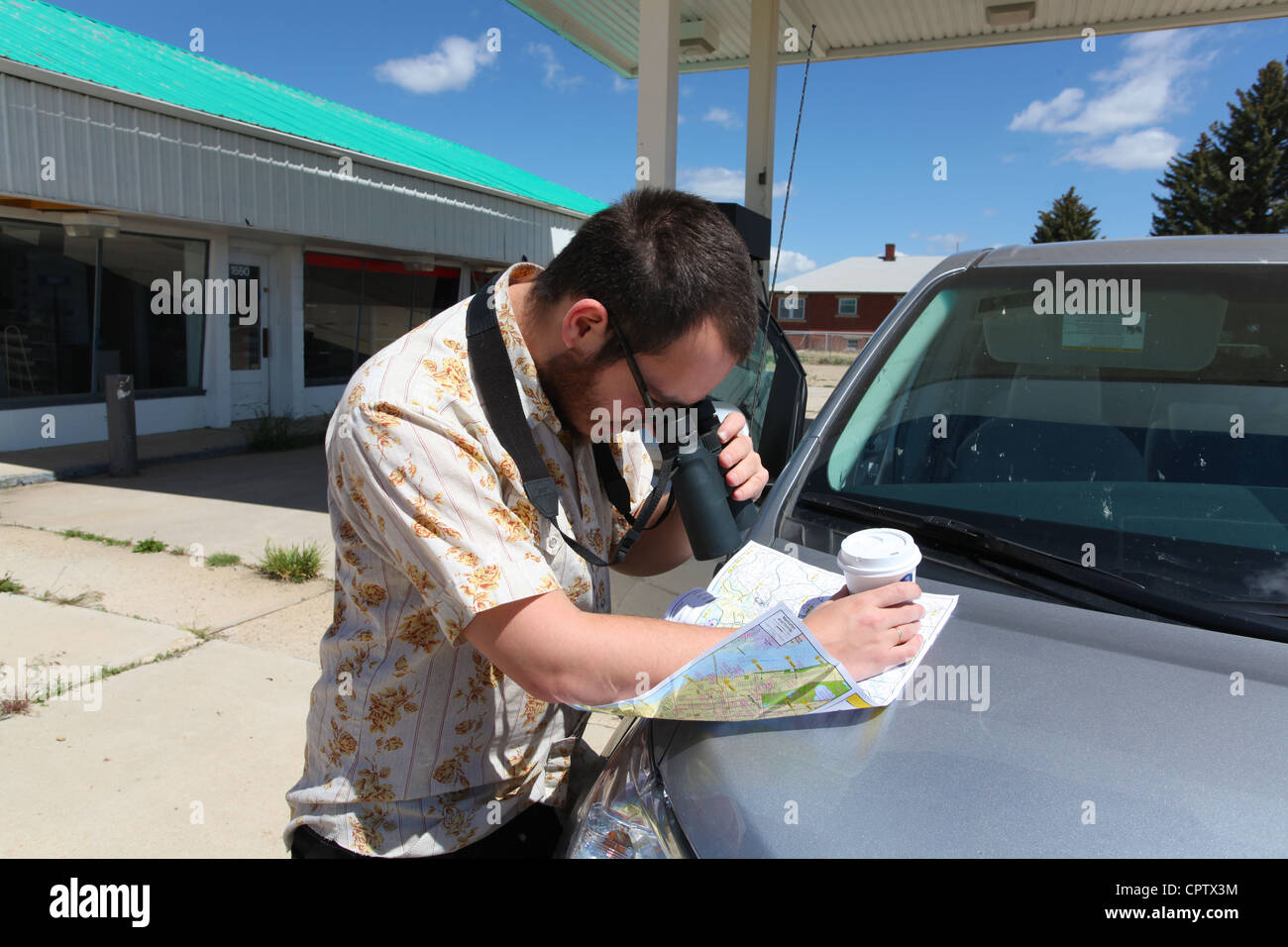 Man studies roadmap with binoculars with abandoned service station in background Stock Photo
