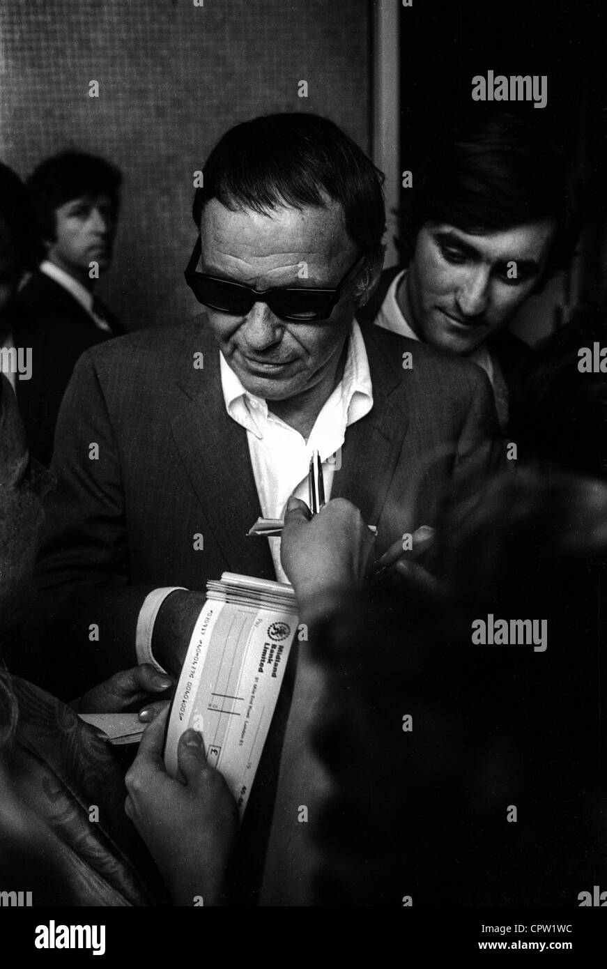 Frank Sinatra writes autographs and somebody in the crowd holds out a pen and a chequebook / checkbook Stock Photo