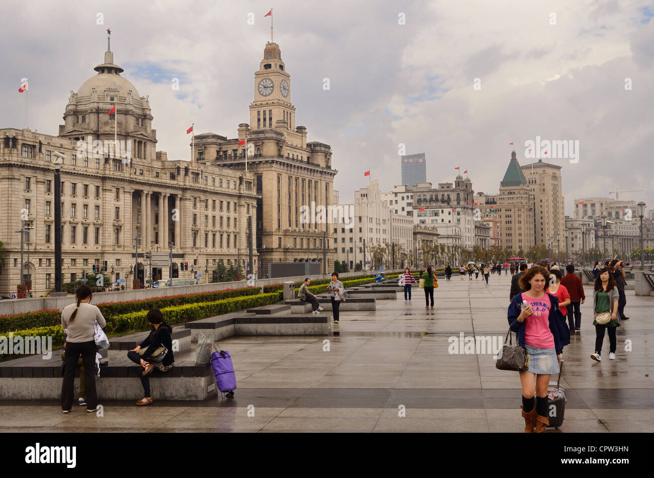 Tourists walking on a wet Bund promenade after a rainstorm with old buildings in Shanghai Peoples Republic of China Stock Photo