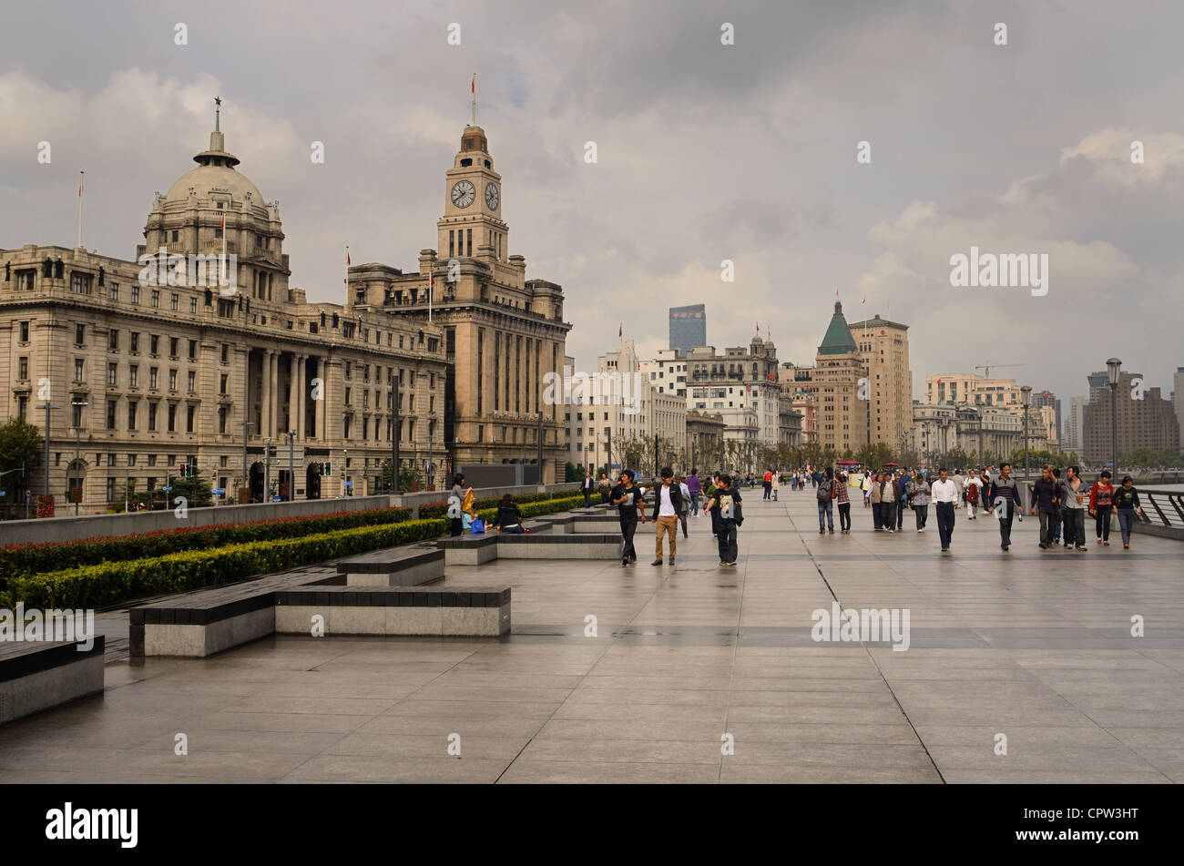 Groups of tourists walking on a wet Bund promenade after a rainstorm with old buildings in Shanghai China Stock Photo