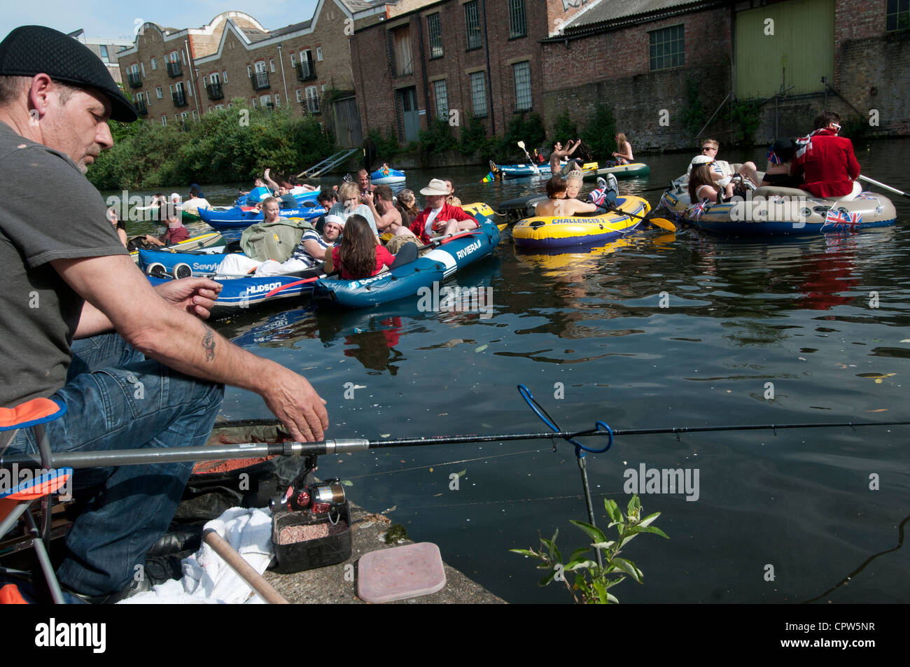 Queen's Jubillegal flotilla floating party, passes a man fishing on Regent's Canal, East London Stock Photo