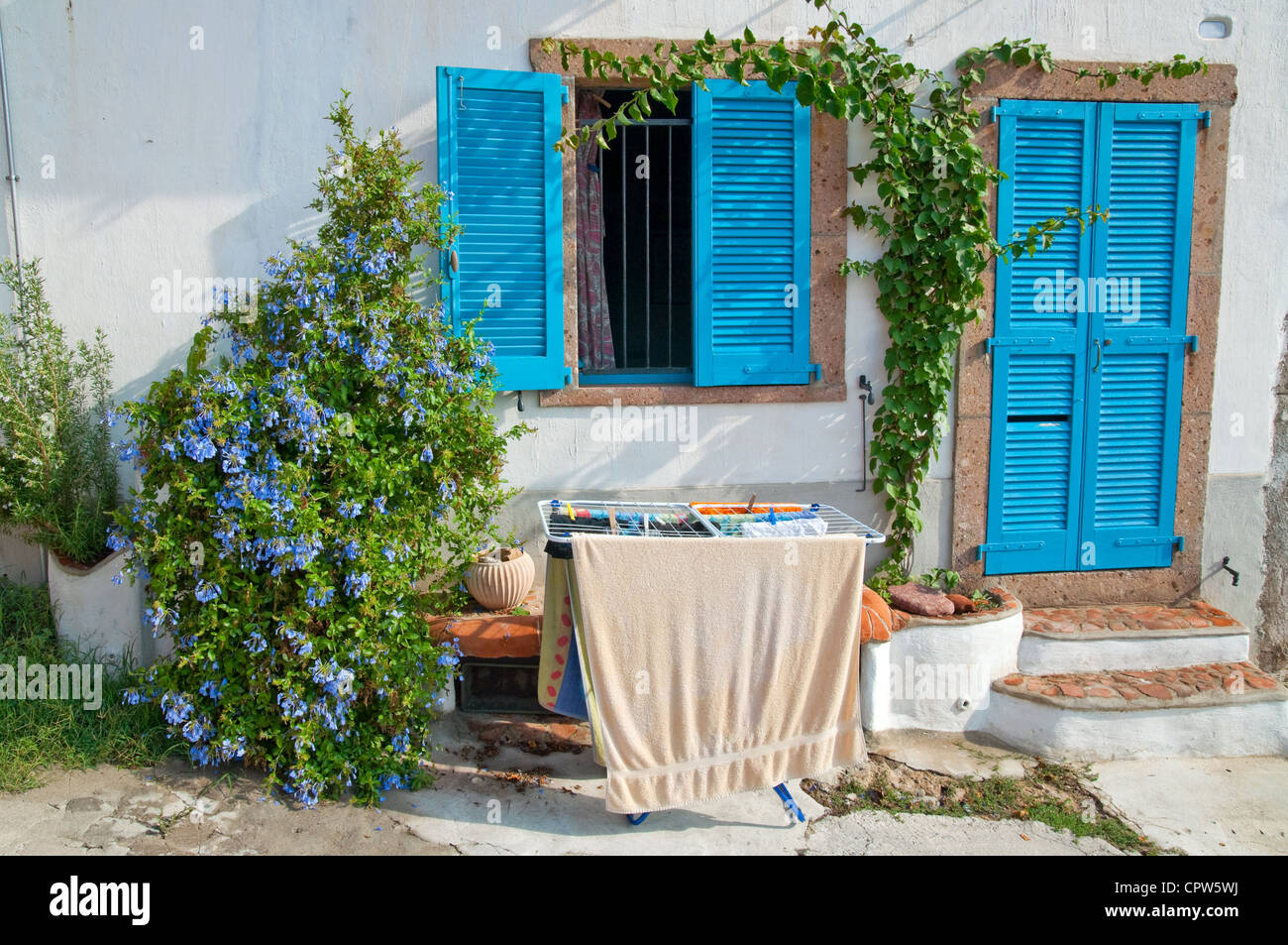 Dryer clothes in front of the Italian village house with a blue door, blue window and blue flowers Stock Photo