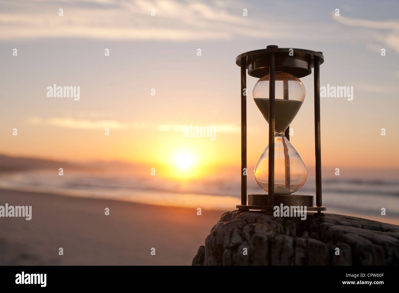 An hourglass on a beach in front of a beautiful sunrise, shallow DOF. Stock Photo