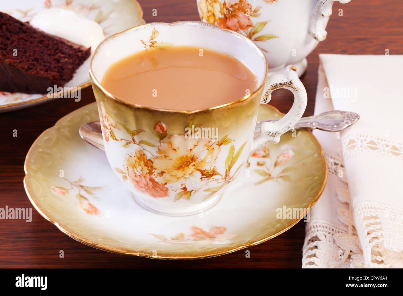 Afternoon tea set out on a dark oak table, with a cup of tea and chocolate cake, delicious nostalgia! Stock Photo