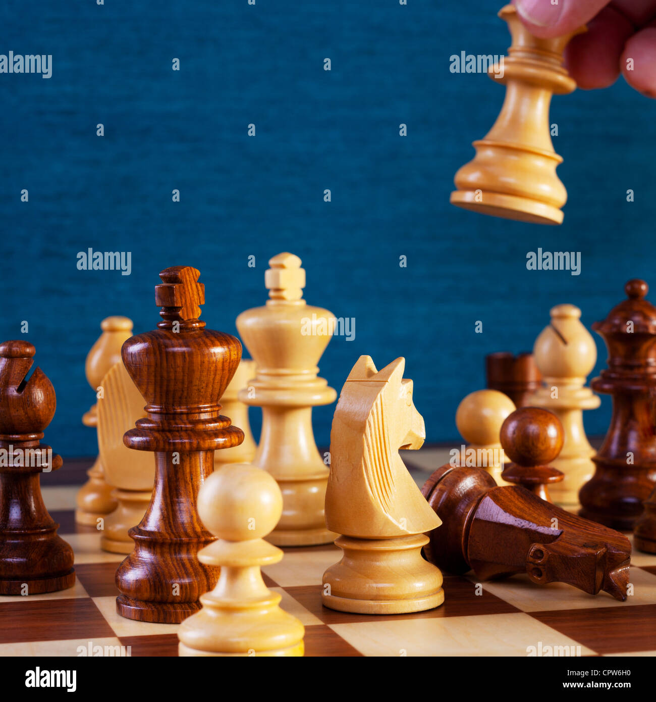 Chess game in progress, white queen is being moved into position, black knight has fallen. Stock Photo