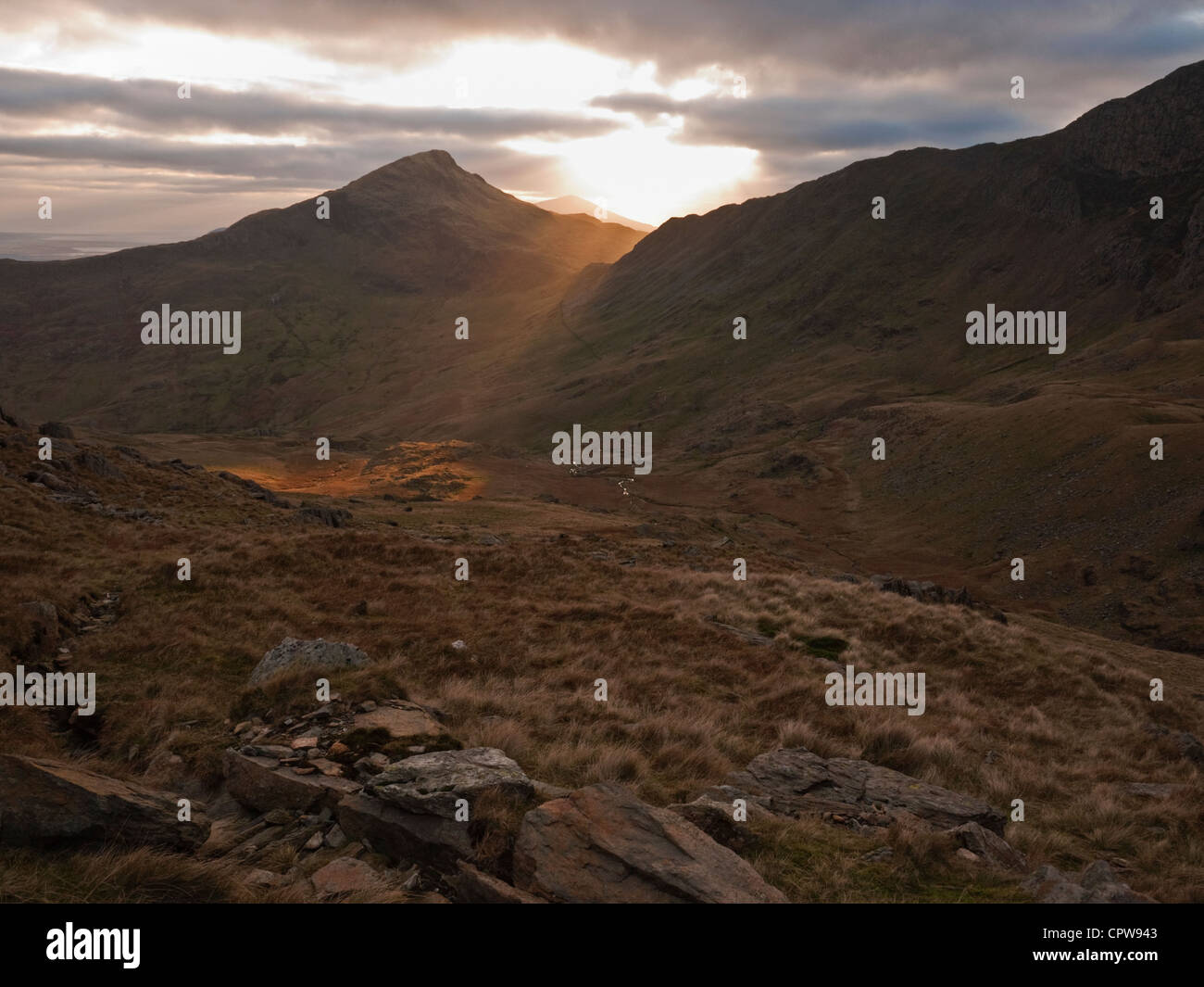 Sun setting behind Yr Aran, a satellite peak of Snowdon viewed from the Watkin Path Stock Photo