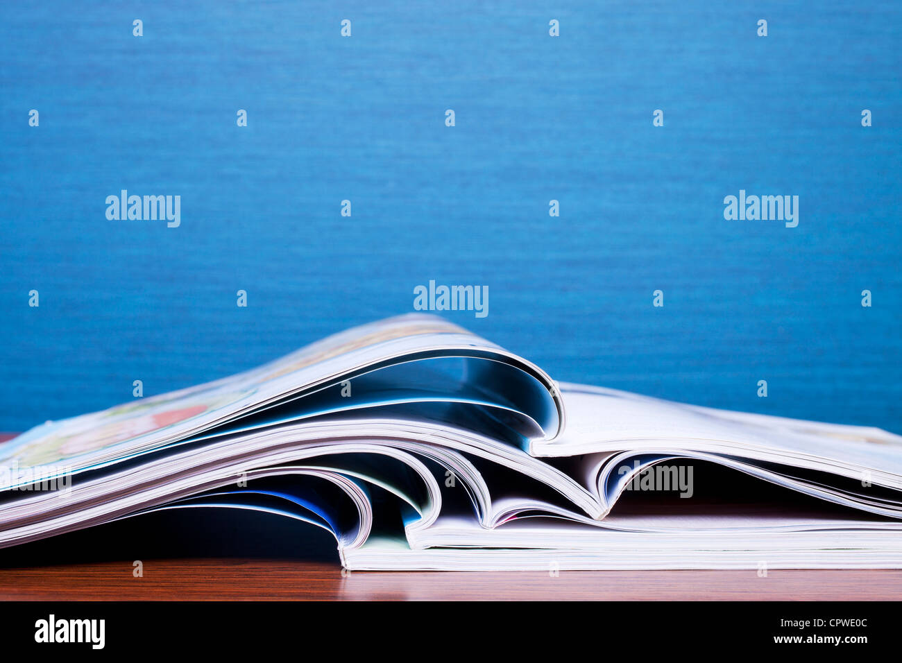Magazines on Table with blue wall behind. Copy space, shallow DOF. Stock Photo