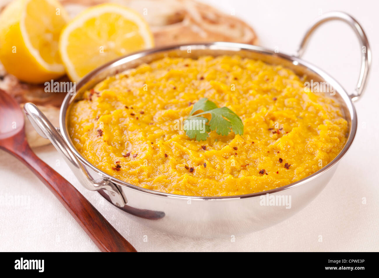 A balti dish filled with tasty Indian dhal or dal, with naan bread and lemon in the background. Shallow DOF focus on foreground. Stock Photo