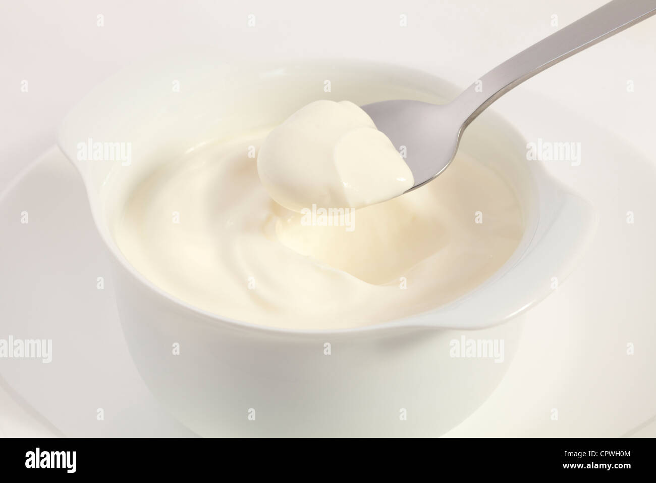 A spoonful of Greek yoghurt being lifted from a bowl. White on white. Stock Photo
