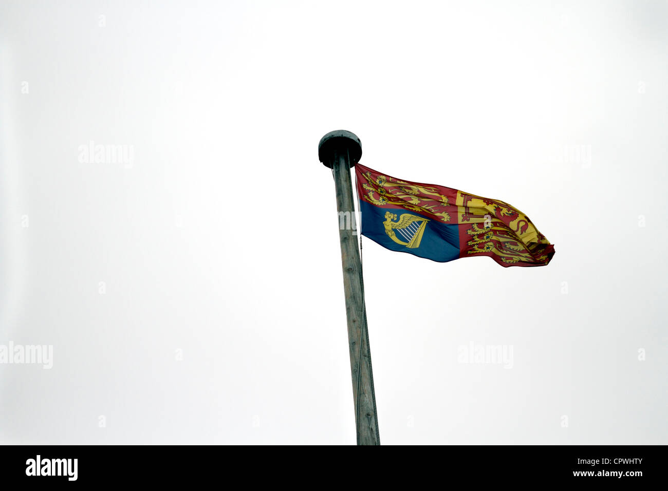 Windsor castle - The Royal Standard, flying as the Queen is in residence. In England, Wales, Northern Ireland, and outside the United Kingdom, the flag is divided into four quadrants. The first and fourth quadrants represent the ancient Kingdom of England and contain three gold lions, (or 'leopards'), passant gardant on a red field; the second quadrant represents the ancient Kingdom of Scotland and contains a red lion rampant on a gold field; the third quadrant represents the ancient Kingdom of Ireland and contains a version of the gold harp from the coat of arms of Ireland on a blue field. Stock Photo