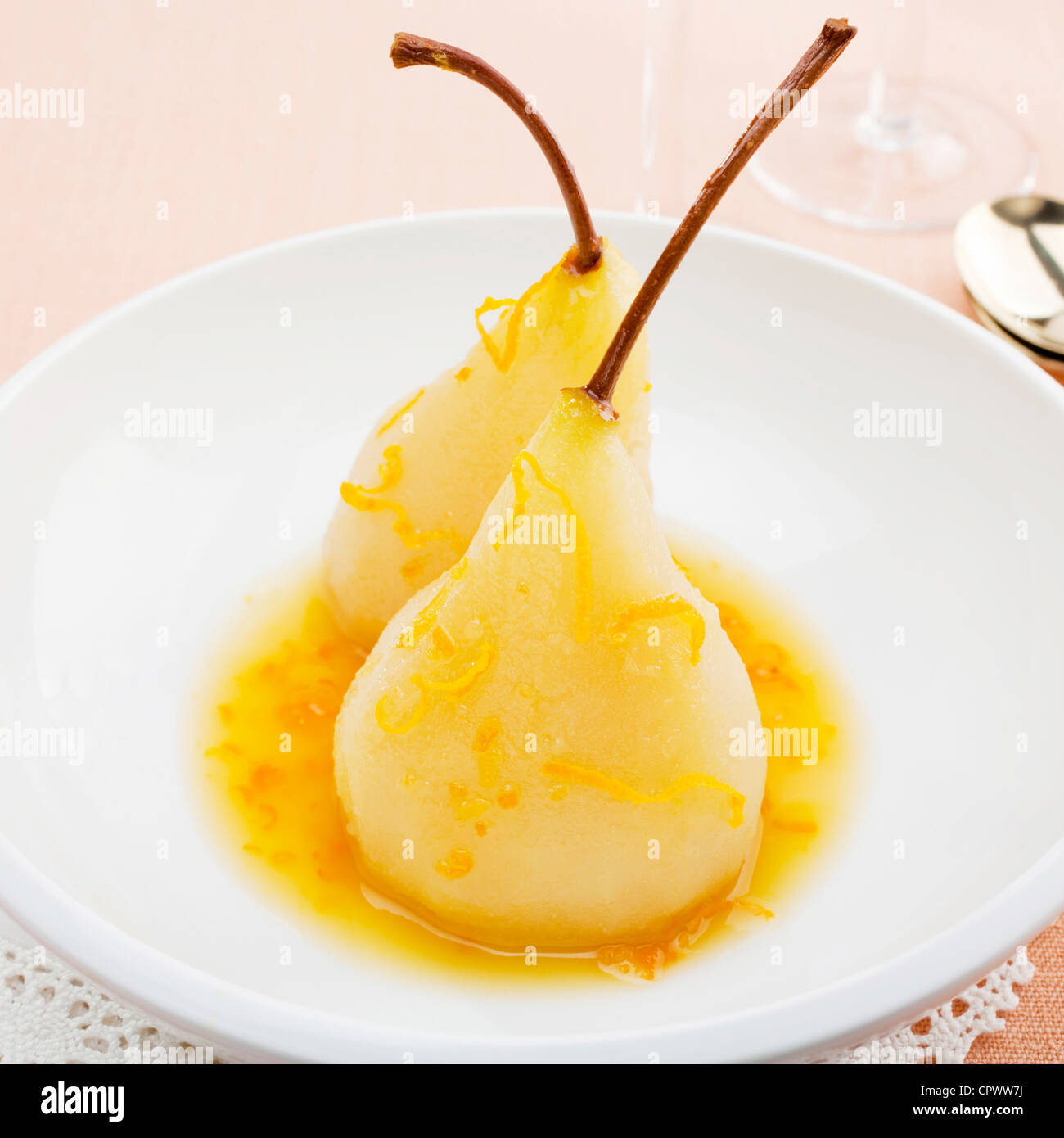 Two pears in a white bowl, poached in orange and lemon juice, garnished with slivers of zest. Stock Photo
