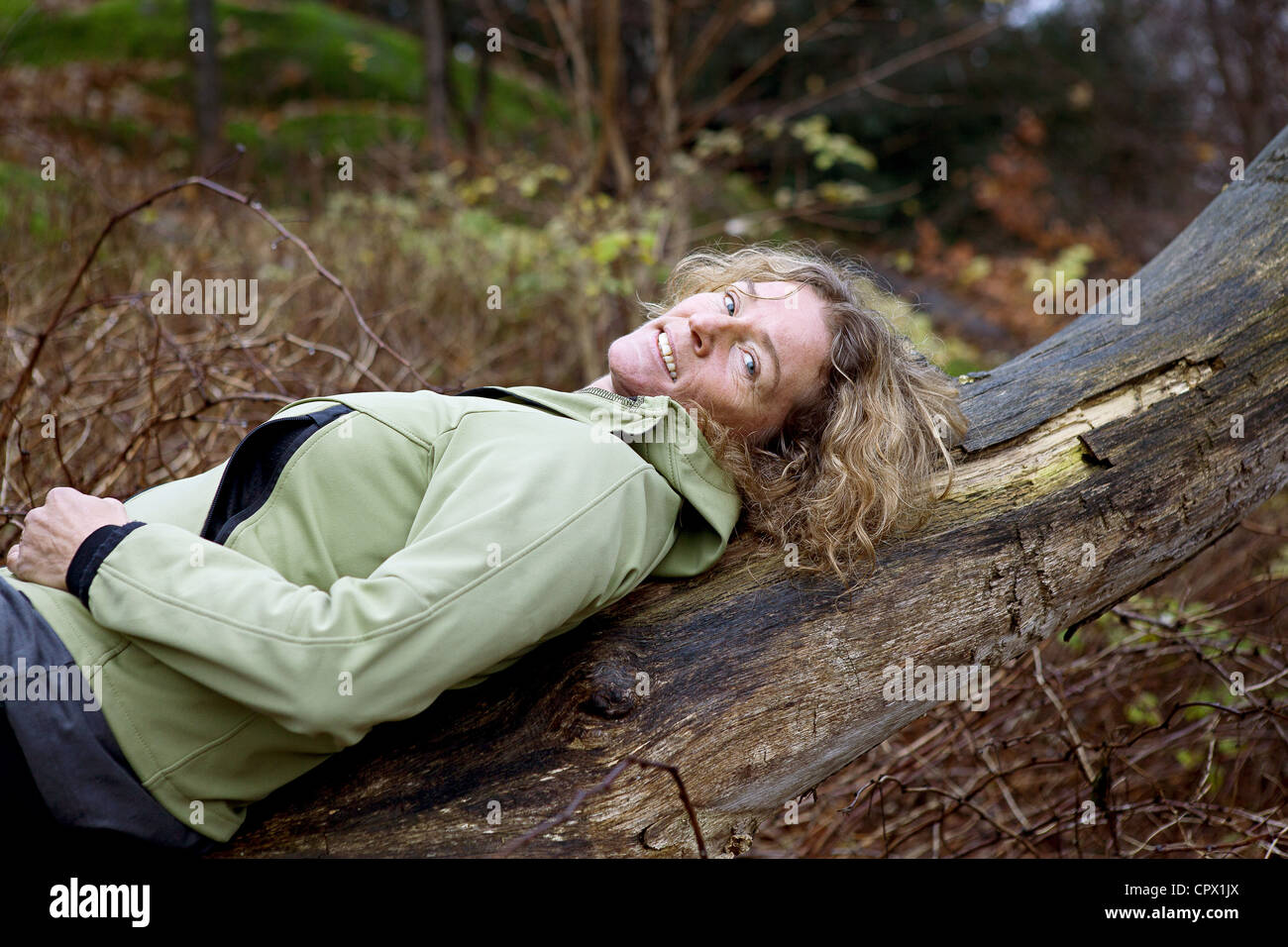 Mature woman resting on tree in forest Stock Photo