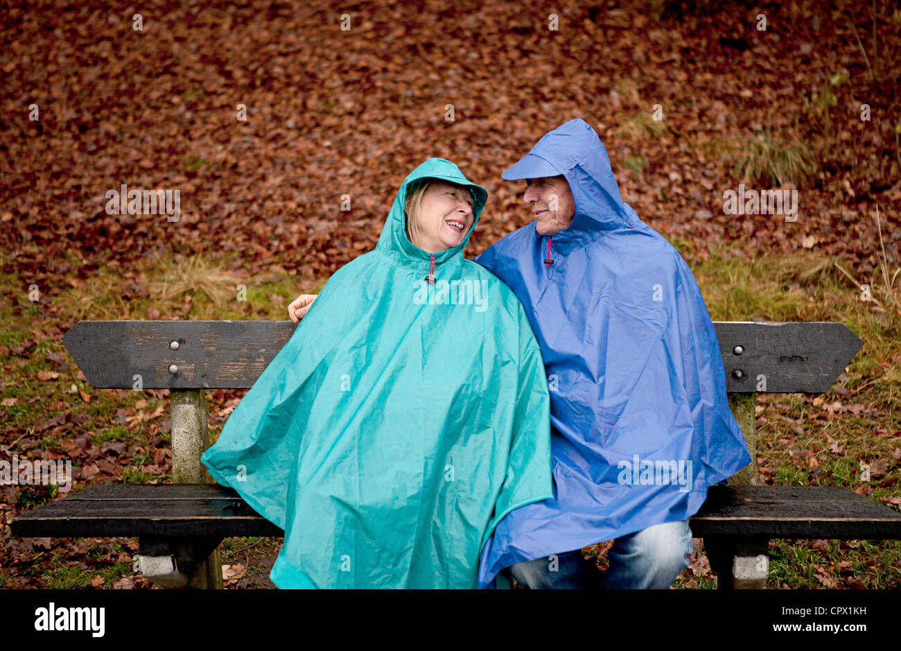 Senior couple sitting on park bench wearing waterproofs Stock Photo - Alamy