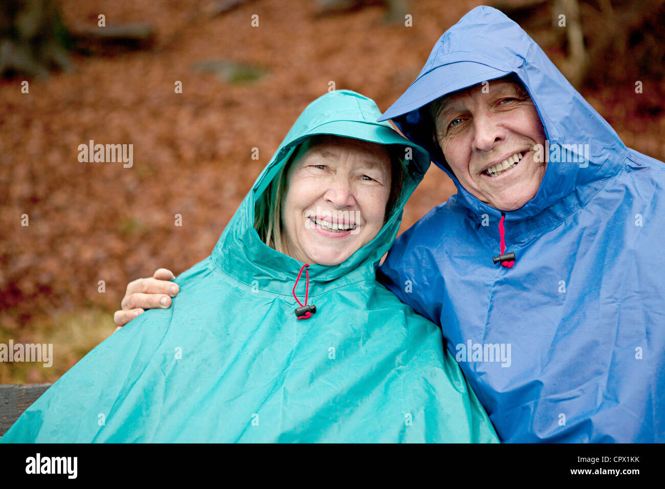 Portrait of senior couple sitting on park bench wearing waterproofs Stock Photo