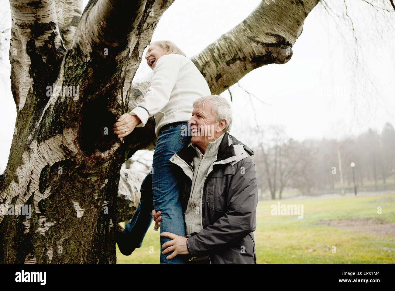 Senior man helping woman climb tree in park Stock Photo