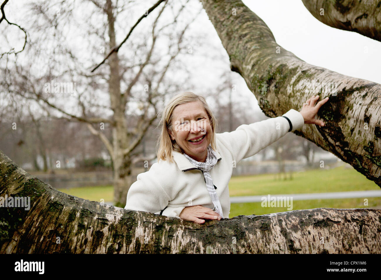 Senior woman leaning against tree, smiling Stock Photo