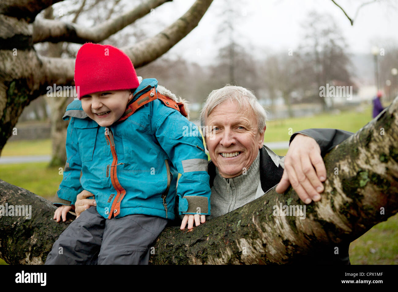 Granfather and boy sitting on tree branch, smiling Stock Photo