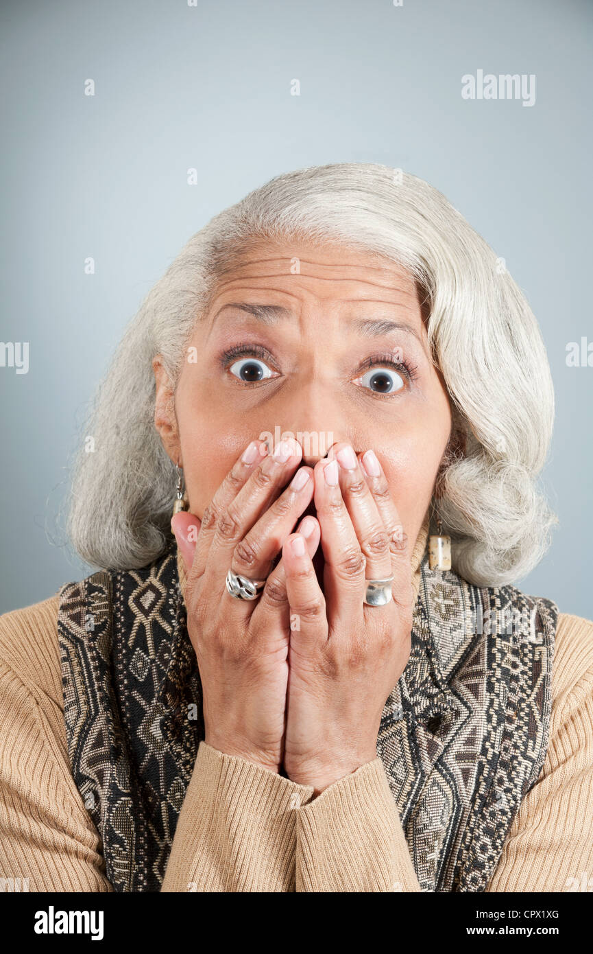 Portrait of senior woman covering mouth with hands in studio Stock Photo