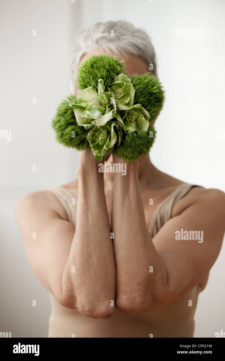 Senior woman holding plant in front of face Stock Photo