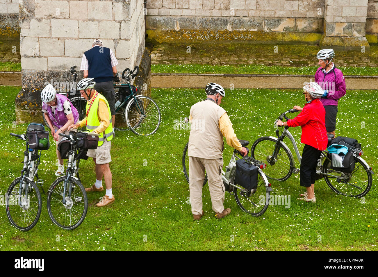 Six older cyclists on holiday parking their bikes on grass - France. Stock Photo