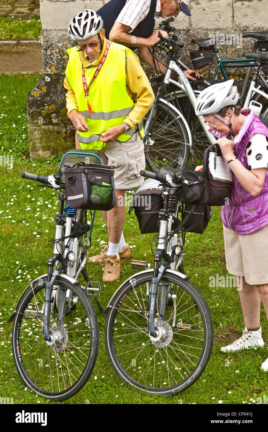 Three older cyclists on holiday parking their bikes on grass - France. Stock Photo