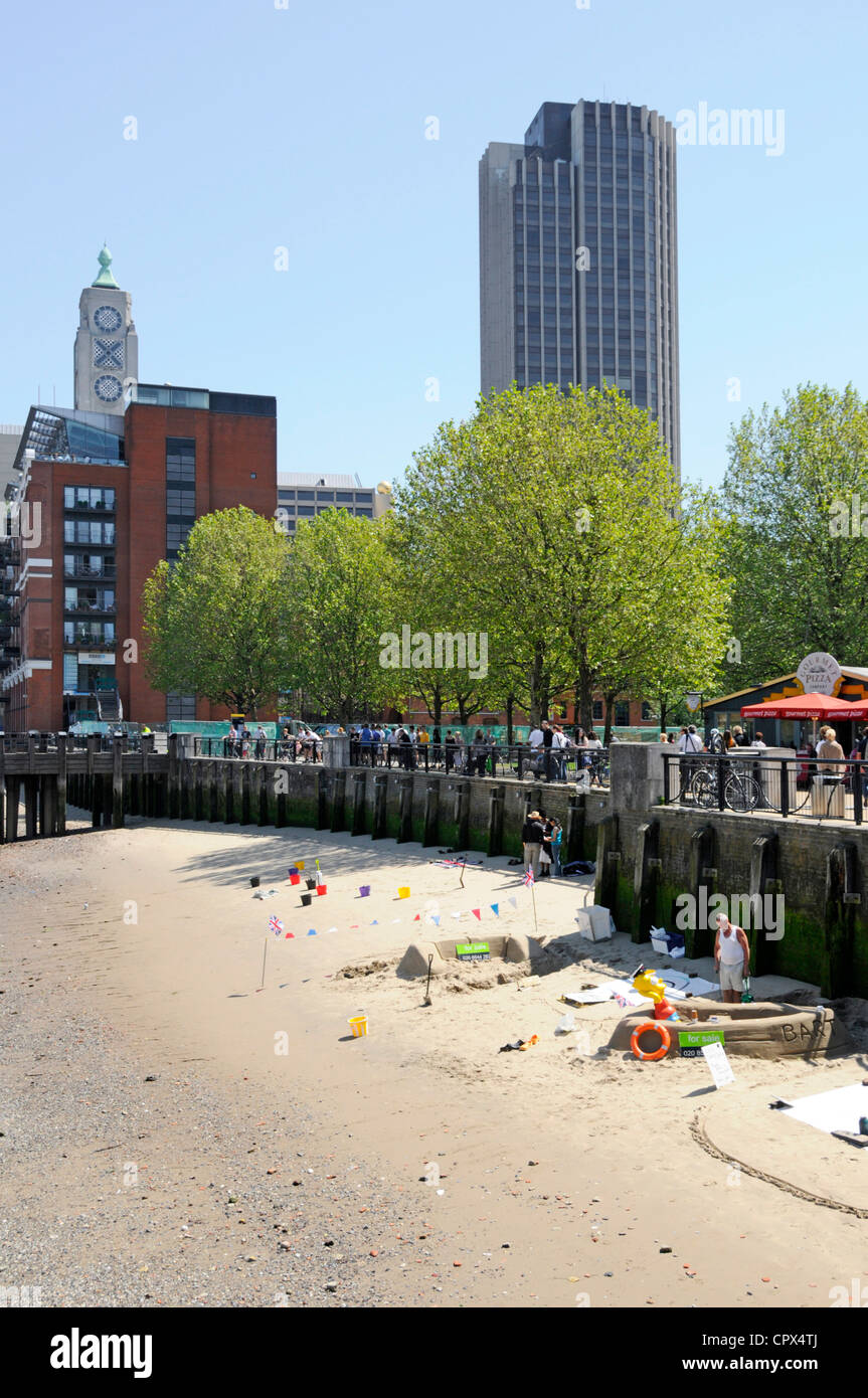 Small area of low tide sandy beach beside River Thames used by men creating sand sculptures hoping for donations from visitors Stock Photo