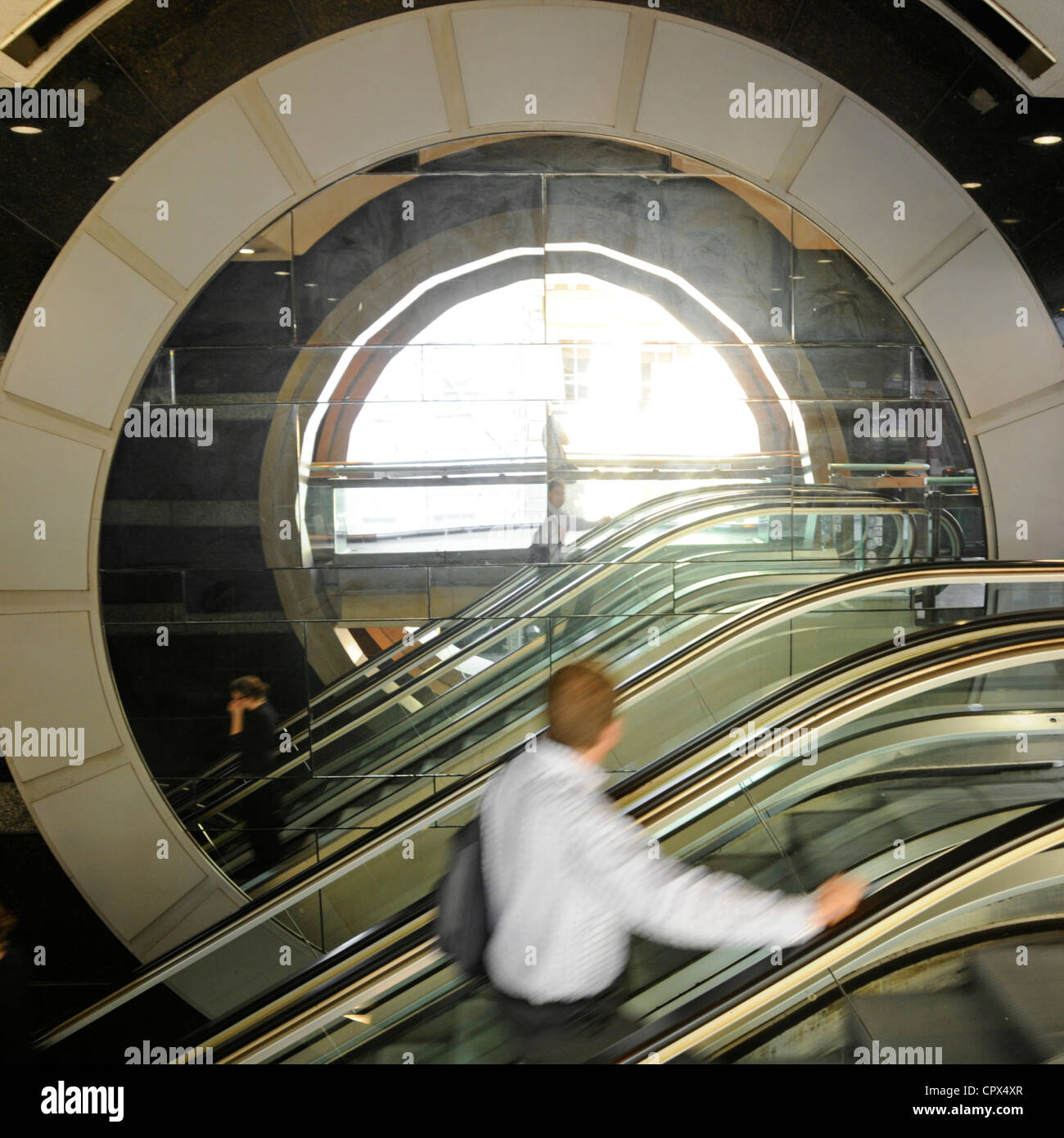 Motion blur of man side view holding on to escalator passing large static circular stone feature Westminster WC2 London England UK Stock Photo