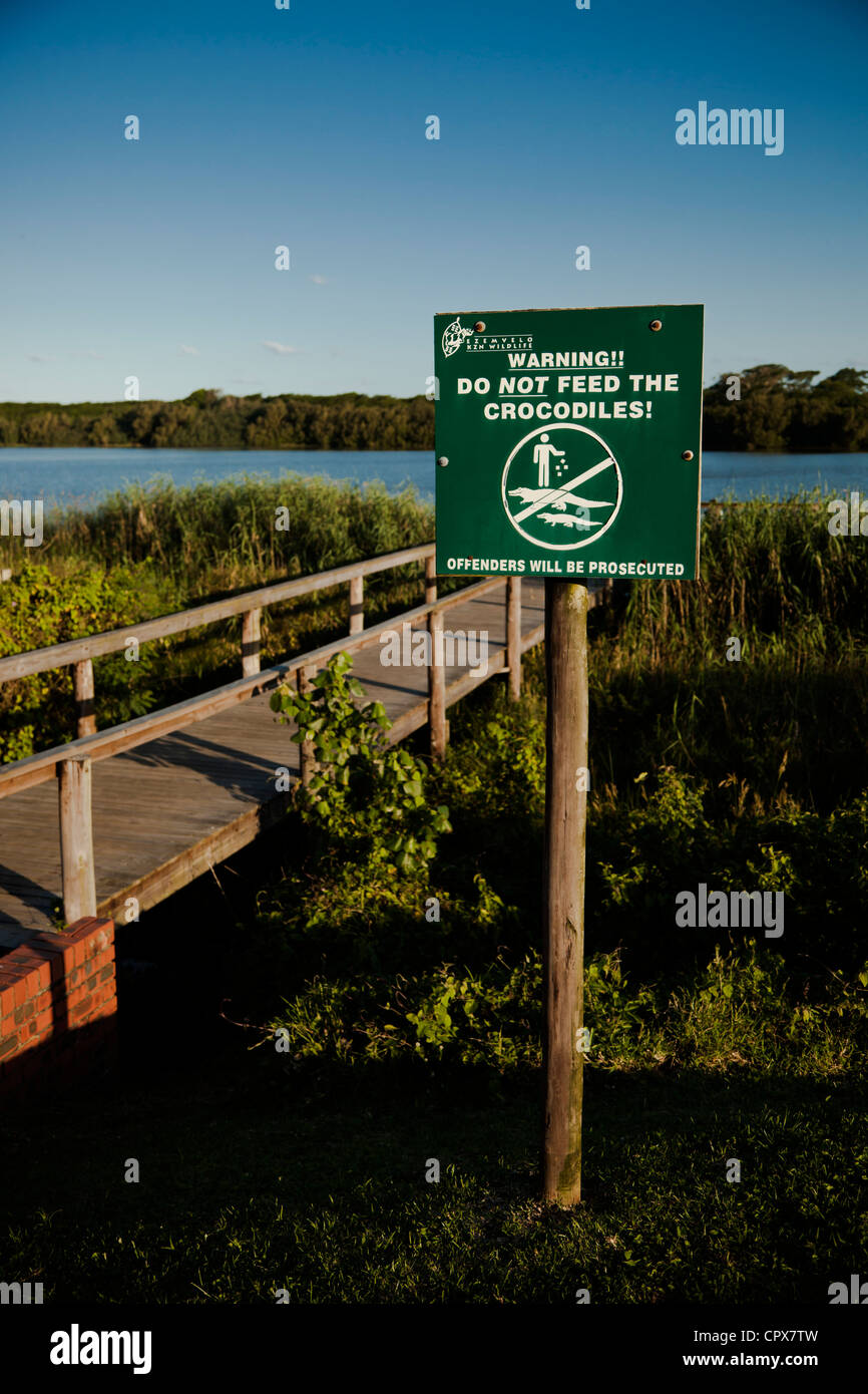 Information sign warning people not to feed crocodiles, with a lake in the background Stock Photo