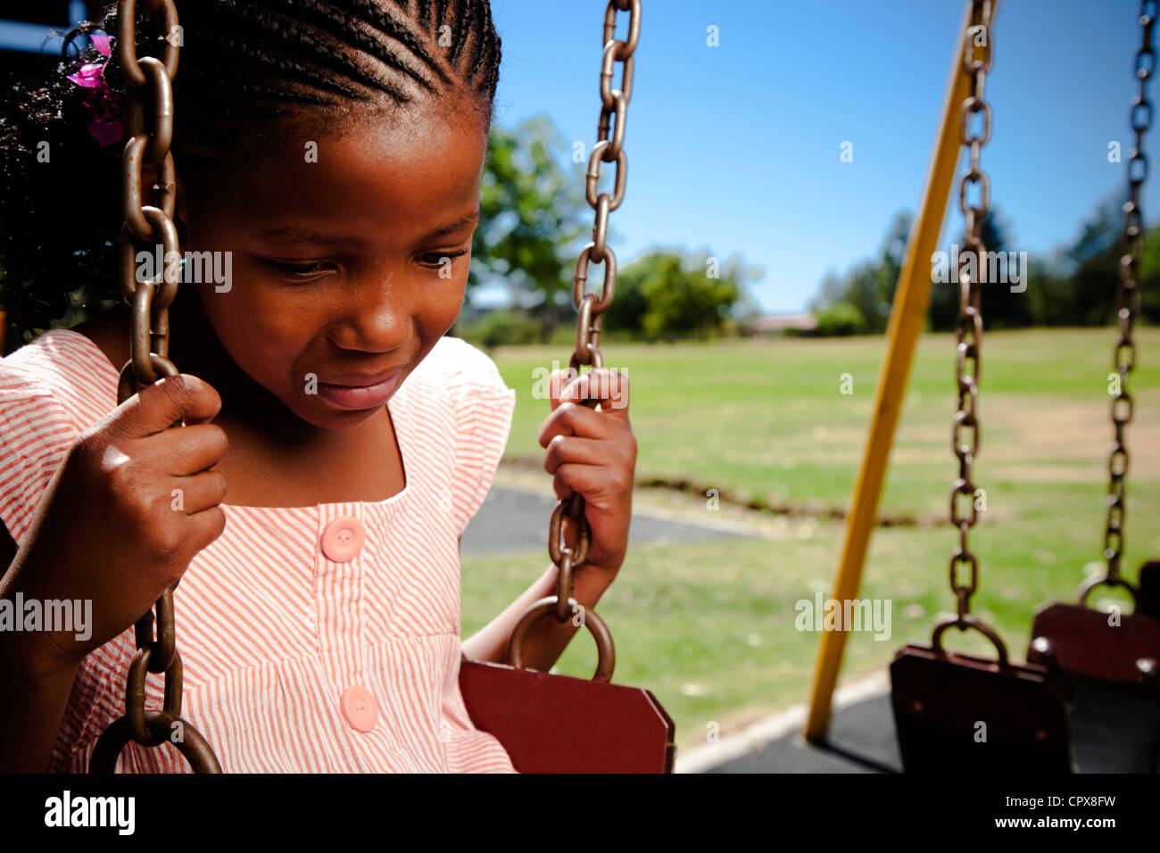 A little girl sitting on a swing looking sad Stock Photo