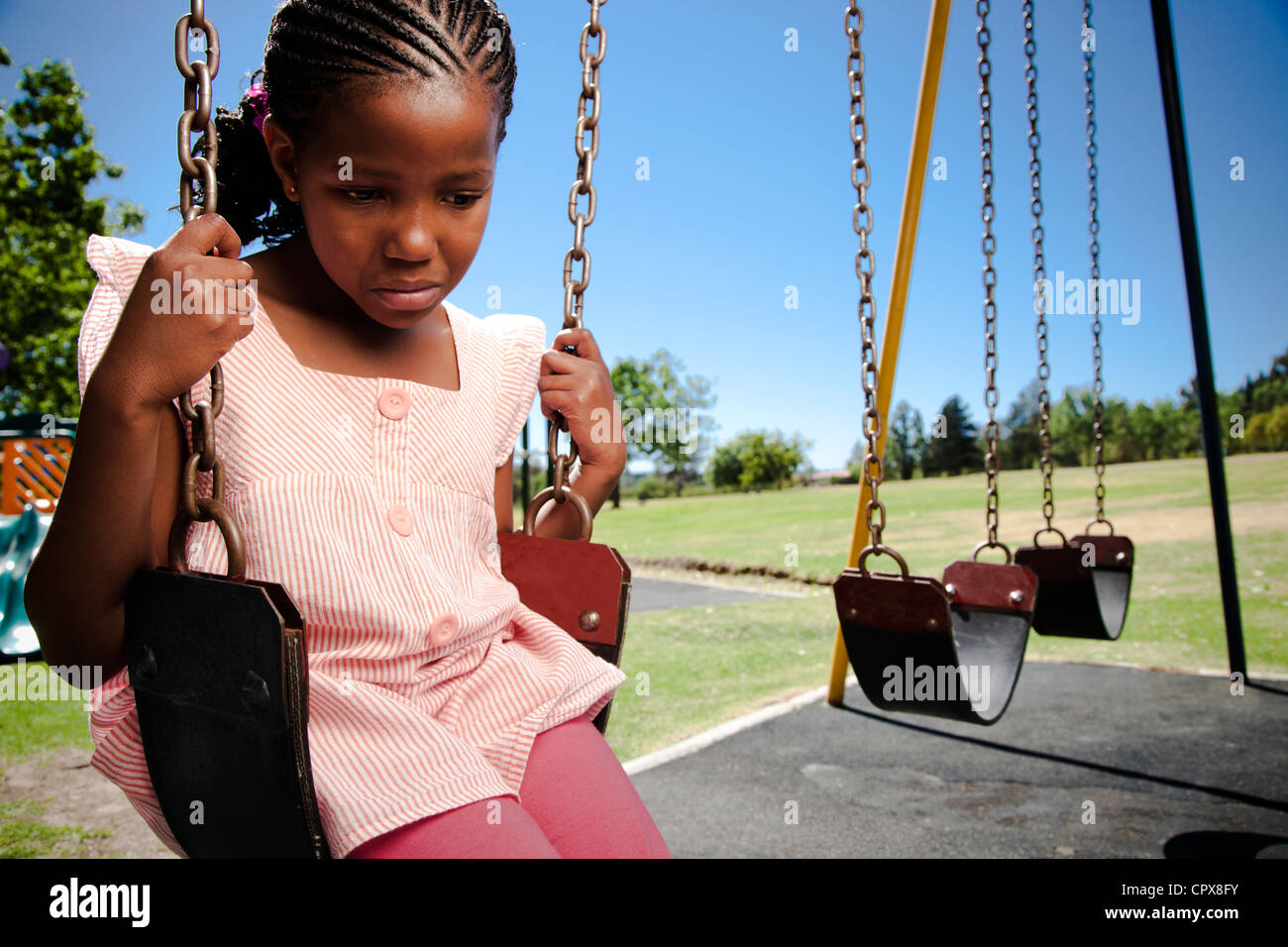 A little girl sitting on a swing looking sad Stock Photo