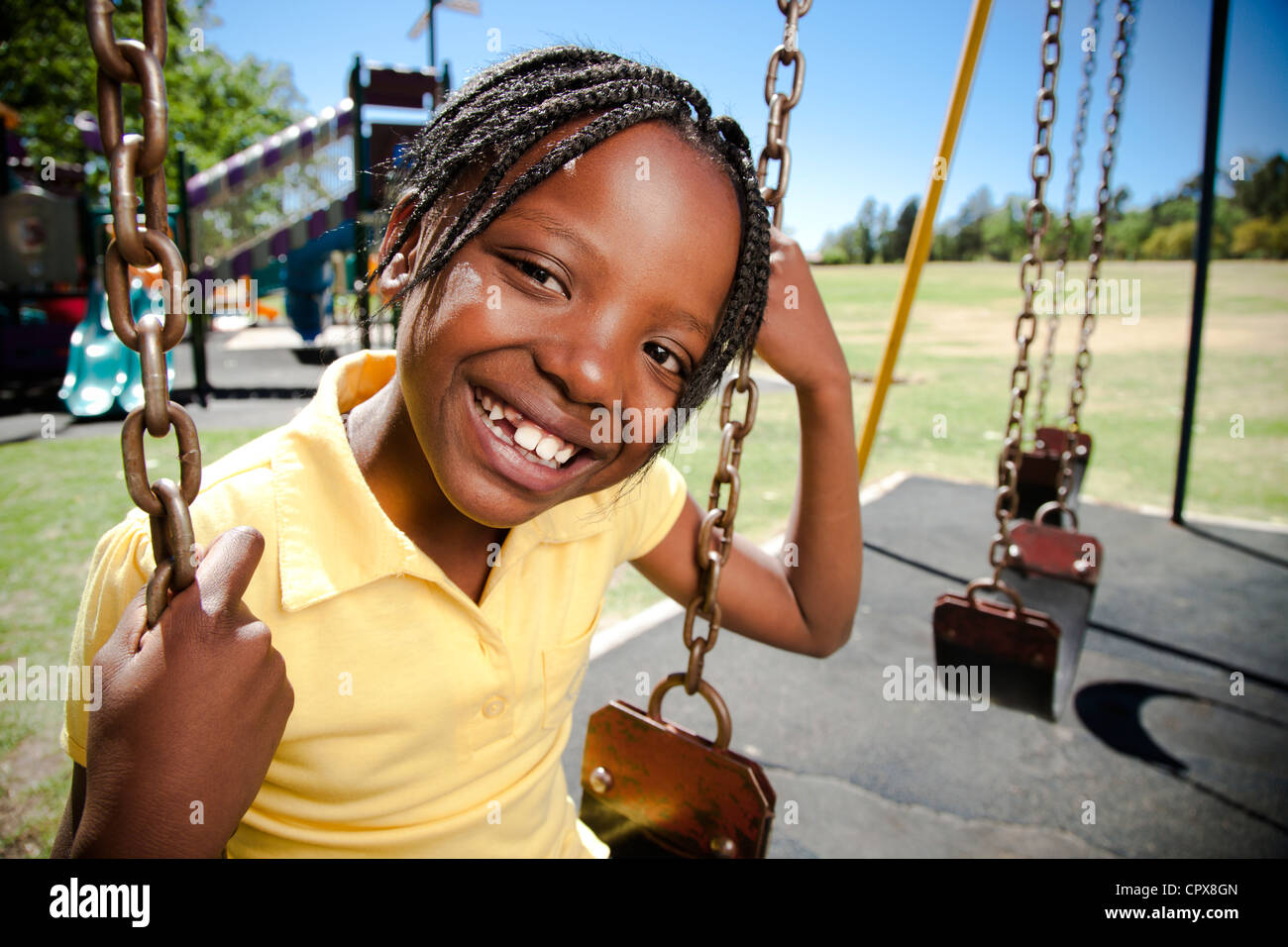 A little girl sitting on a swing smiling at the camera Stock Photo - Alamy